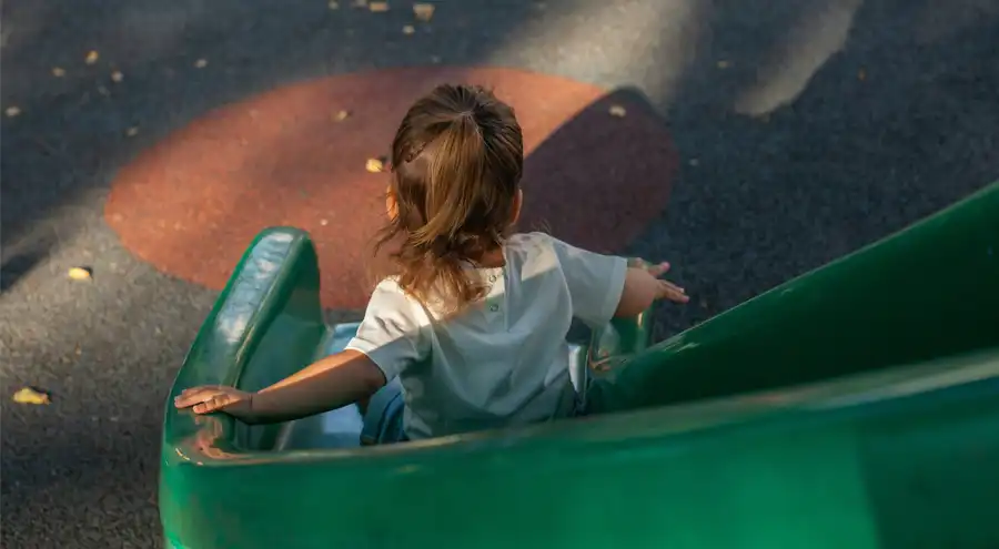 a girl uses a slide on a shady playground
